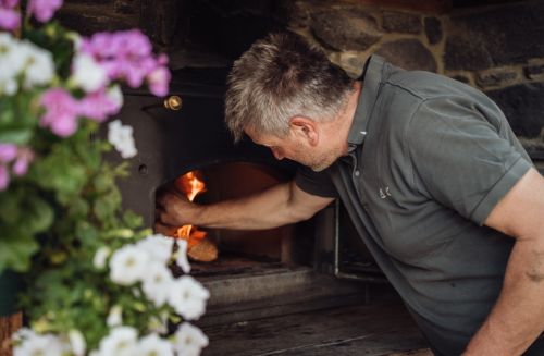 Bauer beim Anheizen des Holzbackofens